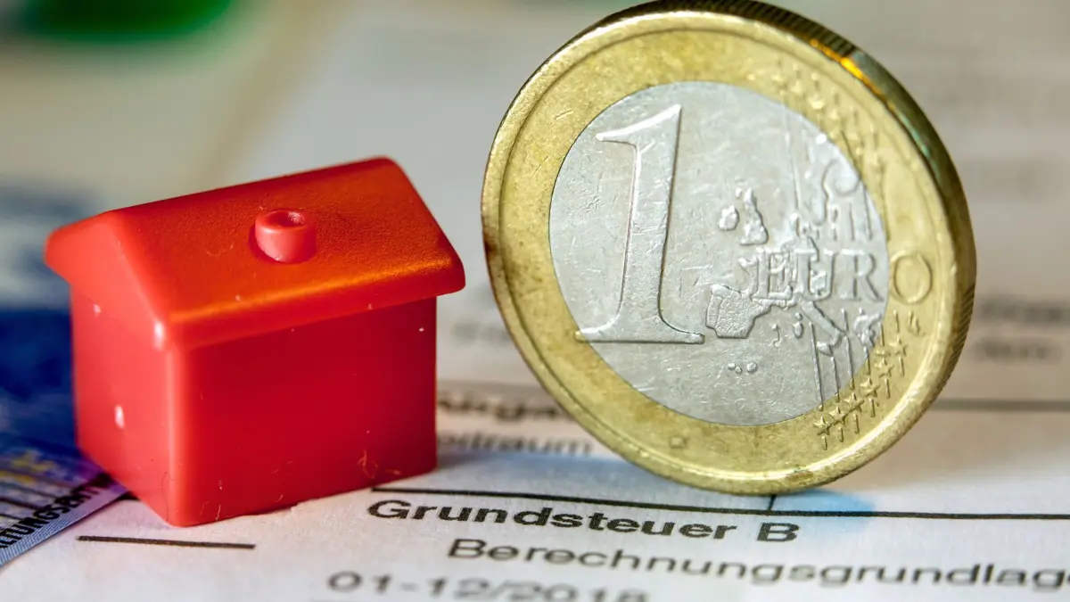 ARCHIV - 30.01.2019, Mecklenburg-Vorpommern, Schwerin: Illustration - Eine Euro-Geldmünze sowie ein Spielzeughaus stehen auf einem Abgabenbescheid für die Entrichtung der Grundsteuer. Drei Wochen nach dem Ende der Abgabefrist fehlen immer noch etwa 1,7 Millionen Grundsteuererklärungen säumiger Immobilieneigentümer bei den Finanzämtern in Nordrhein-Westfalen. Rund fünf Millionen Grundsteuererklärungen seien mit Stand Dienstag bisher eingegangen, sagte ein Sprecher der Oberfinanzdirektion (OFD) Nordrhein-Westfalen der Deutschen Presse-Agentur. (zu dpa: «Immer noch fehlen etwa 1,7 Millionen Grundsteuererklärungen») Foto: Jens Büttner/ZB/dpa +++ dpa-Bildfunk +++