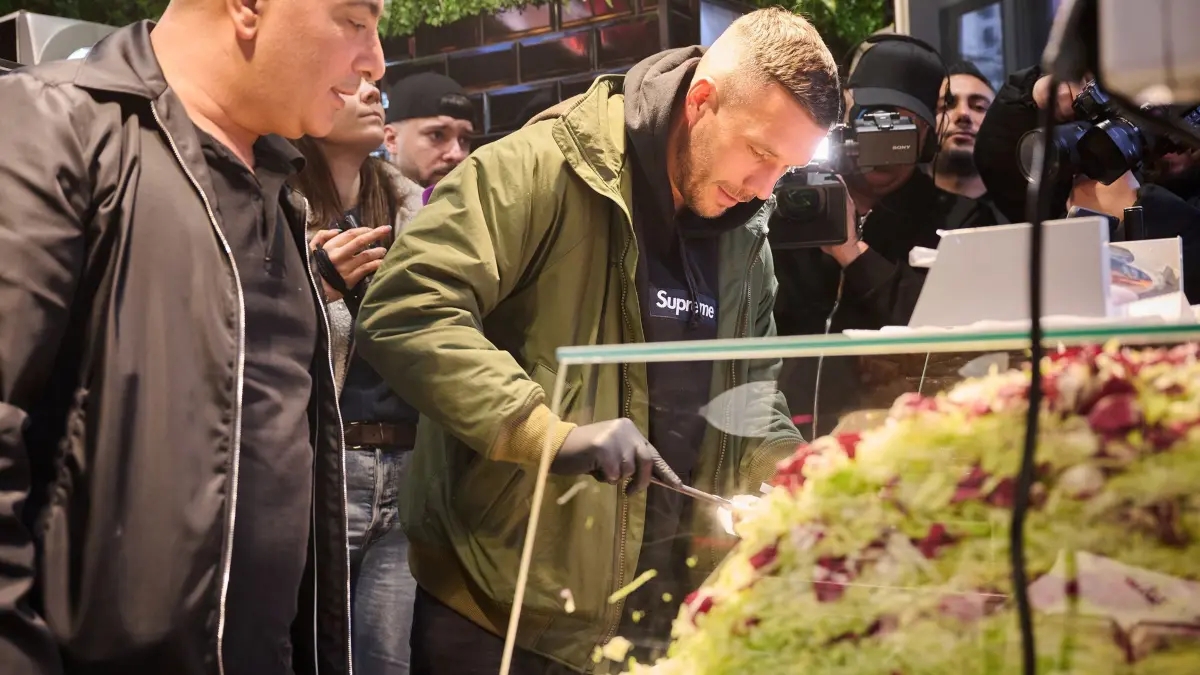 Lukas Podolski (r), ehemaliger Fußballprofi und Unternehmer, und Metin Dag belegen einen Döner während der Eröffnung von Podolskis Döner–Imbiss.