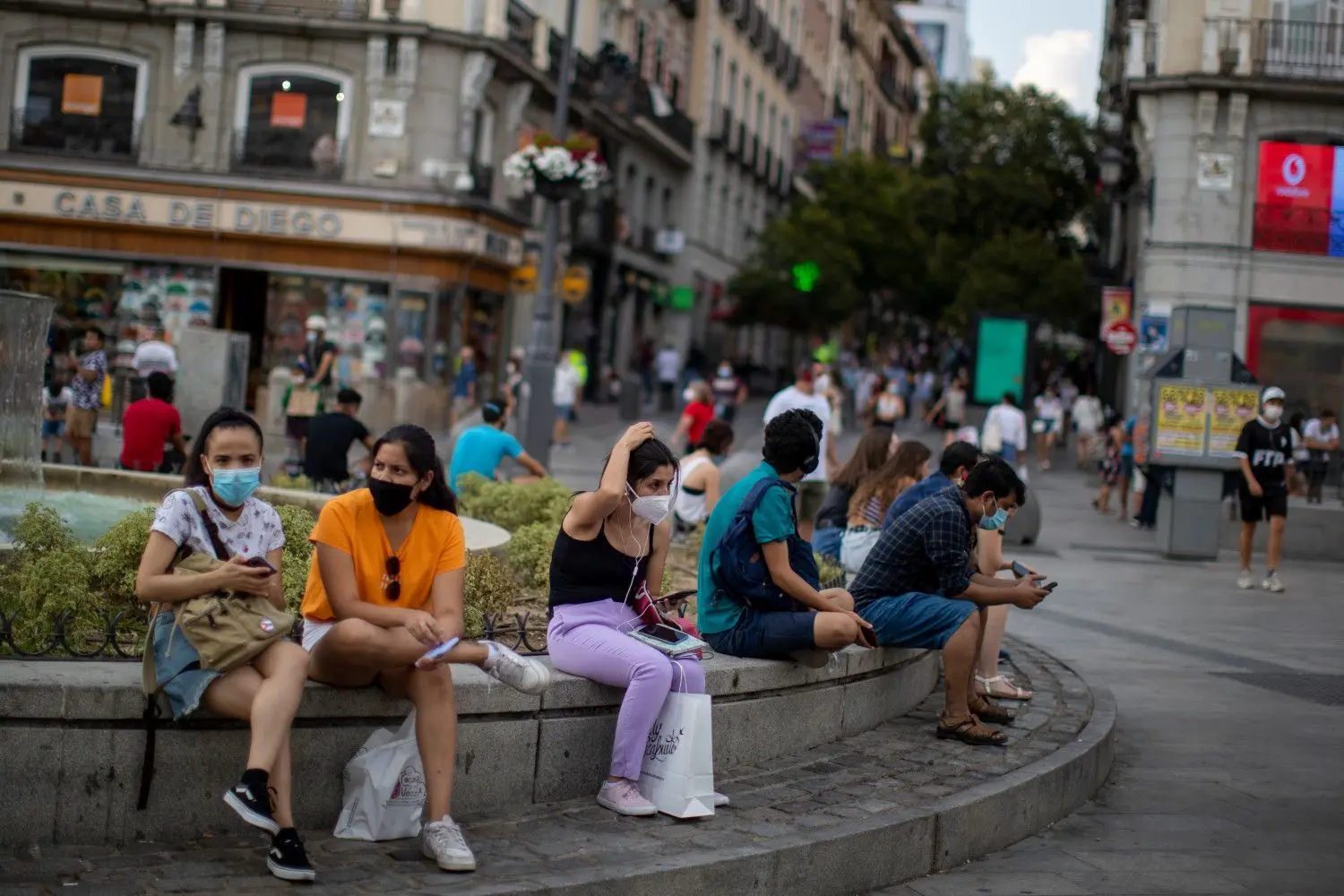 Menschen mit Masken sitzen auf einer Straßenbank in Madrid. Das Auswärtige Amt warnt wegen der Corona-Pandemie nun auch vor Reisen in Spaniens Hauptstadt und ins spanische Baskenland.