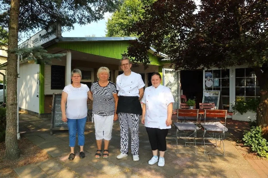 Bäume spenden Schatten im Lokal-Garten: das aktuelle Team vom Doppelpunkt mit Carola Laack, Hannelore Klatt, Mike Bader und Annette Siebmann. Links ist der Imbissstand zu sehen, rechts der Eingang zum Gastraum.