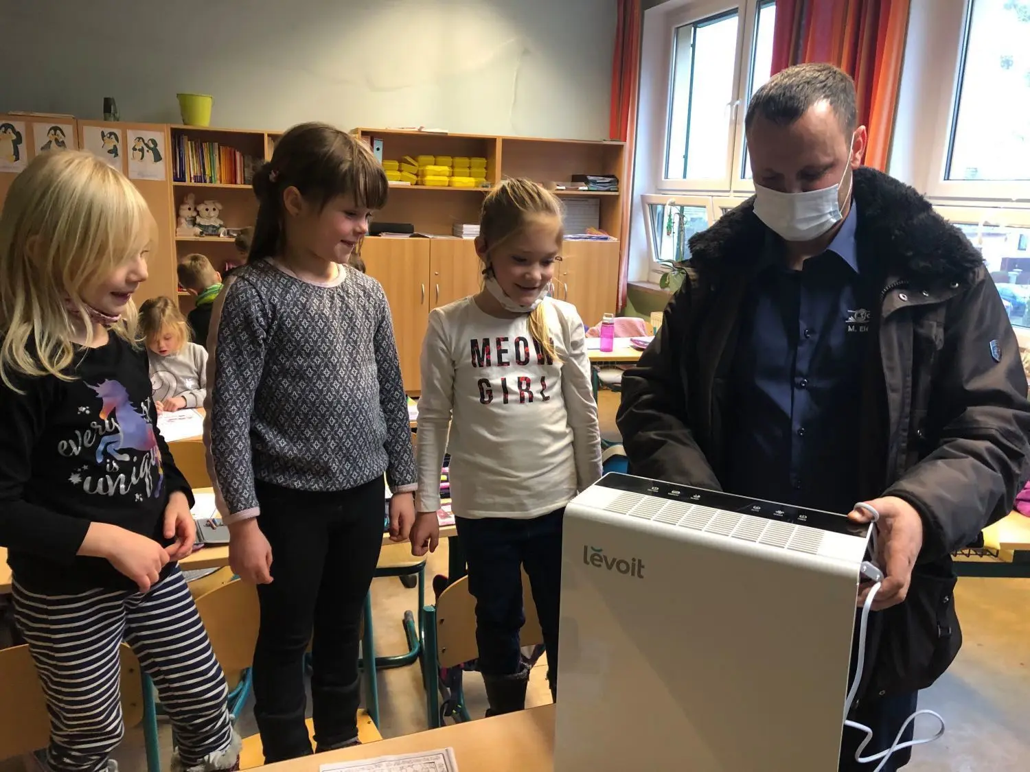 Neugierig auf den Neuen  im Klassenzimmer: Milena Lust (v.l.), Johanna Eichendorff und Lia Ladewig aus der 1b in Britz  lassen sich von Johannas Papa Michael Eichendorff den Luftreiniger erklären. Das Gerät - eine Firmenspende der Reifen- und Autoservice Slowinski GmbH - soll aus der Luft im Klassenraum mehr als 99 Prozent der Viren wegfiltern.