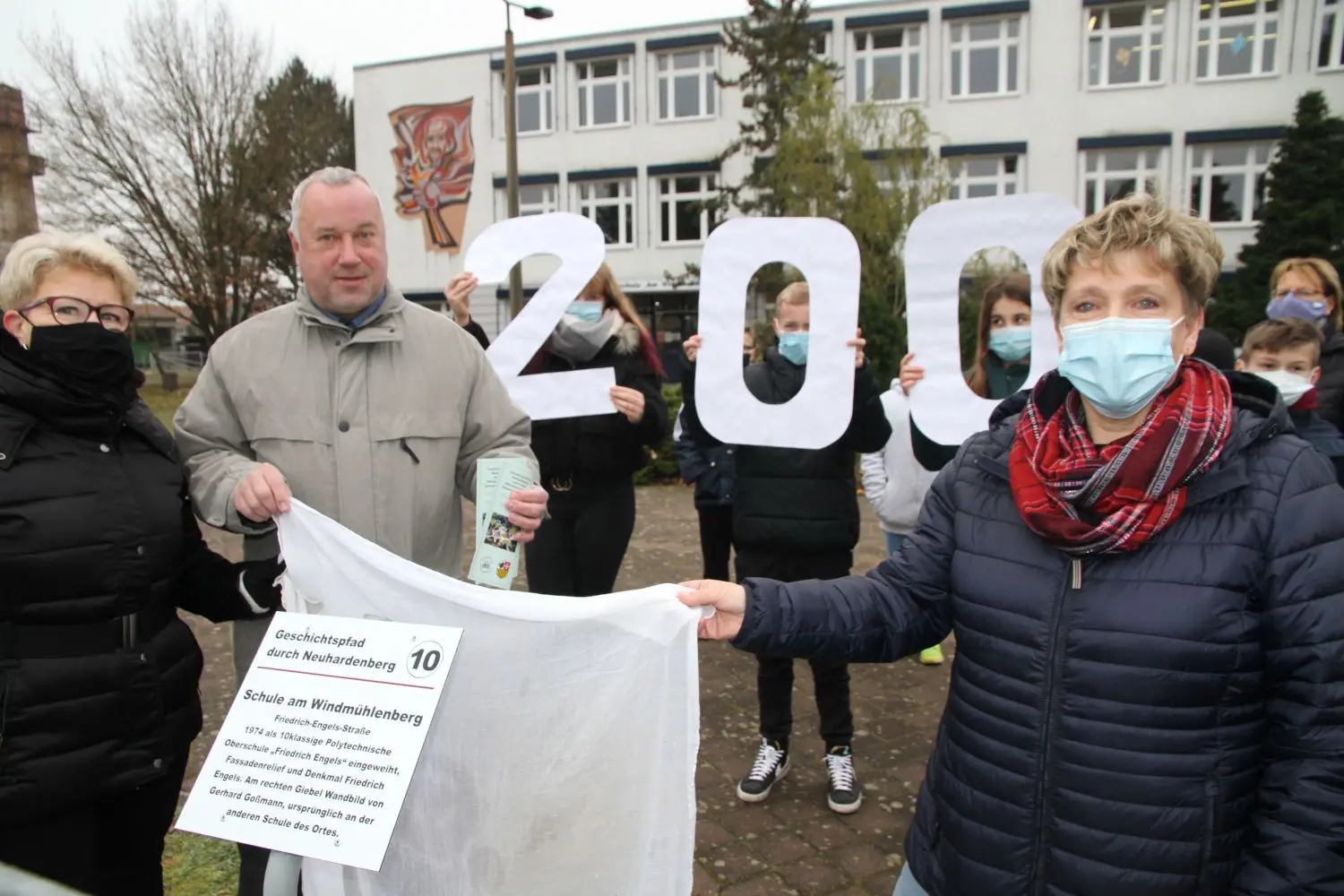 Feierlich: Amtsausschuss-Chefin Cornelia Korbanek, Heimatvereinschef-Dietmar Zimmermann und Schulleiterin Petra Arendt (vl.) haben gemeinsam mit Klassensprechern der Schule am Mittwochvormittag an der einstigen Friedrich-Engels-Grundschule in Neuhardenberg die neue Tafel des Geschichtspfads anlässlich des bevorstehenden 200. Engels-Geburtstags am Zaun der Schule enthüllt.