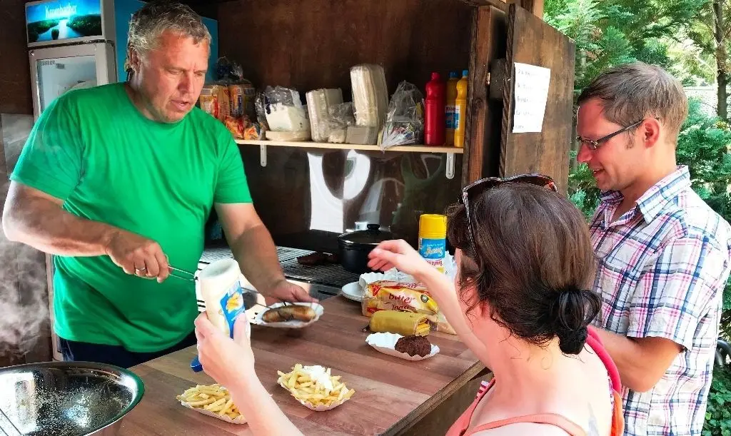 Gästeversorgung im Akkord am Großen Müllroser See: Enrico Schenk grillt in der Imbiss-Holzhütte Buletten und Bratwürste und bedient hier Karolin Falkenhain und Nico Wolff aus Neuhardenberg, für die er auch knusprige Pommes frites zubereitet hat.