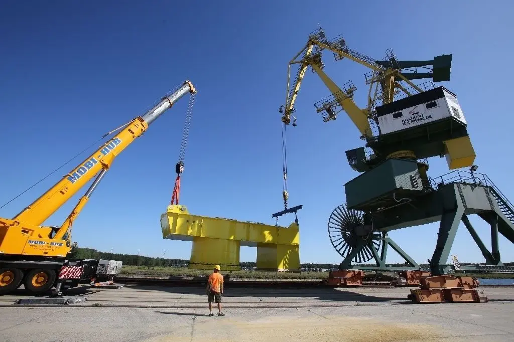 Präzisionsarbeit mit tonnenschwerer Last: Absolut synchron hieven der Mobil- und der Umschlagskran (letzterer ebenfalls aus dem Kranbau Eberswalde) das Mittelstück der Plattform auf das Schiff im Binnenhafen.