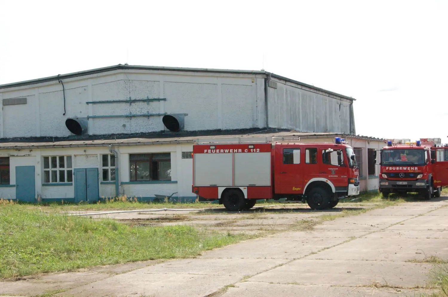 Das Haus, dem die brennede Batteriezelle stand, wurde zerstört. Im Vordergrund Feuerwehrfahrzeuge, die dekontaminisert werden mmussten. Das Gebäude war früher eine Reparaturwerkstatt für Jagdflugzeuige