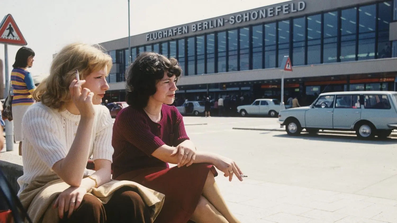 Tor zur Welt: Zwei junge Frauen sitzen im Jahre 1977 rauchend vor dem neuen Flughafen-Gebäude von Berlin-Schönefeld.