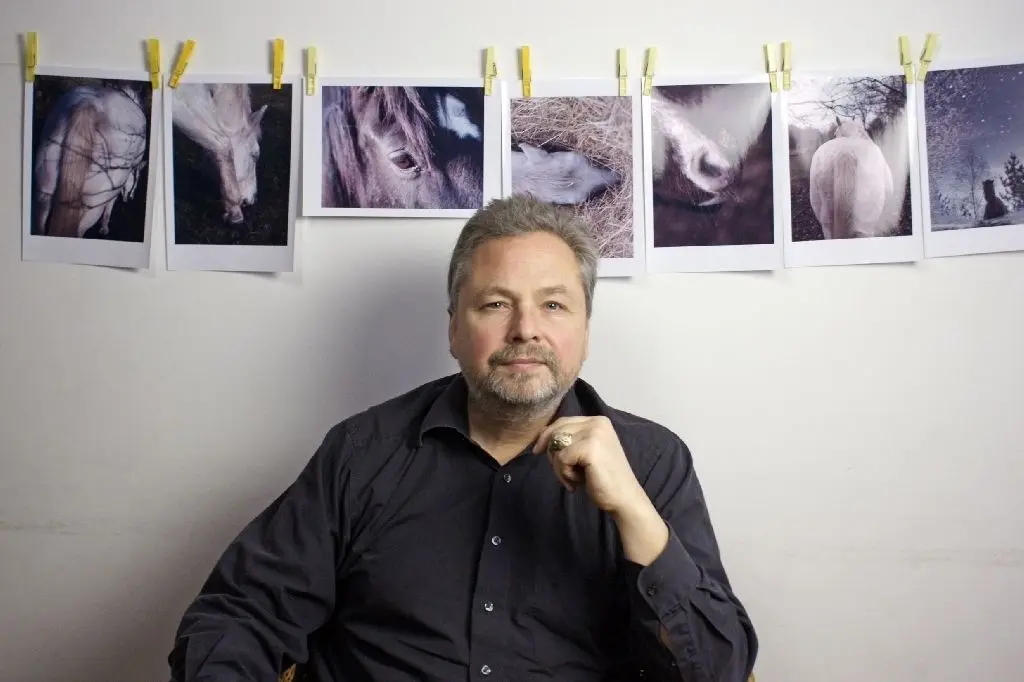 Neues Projekt: Fotograf Fred Hüning vor einer Wand mit einer Serie von Pferdebildern