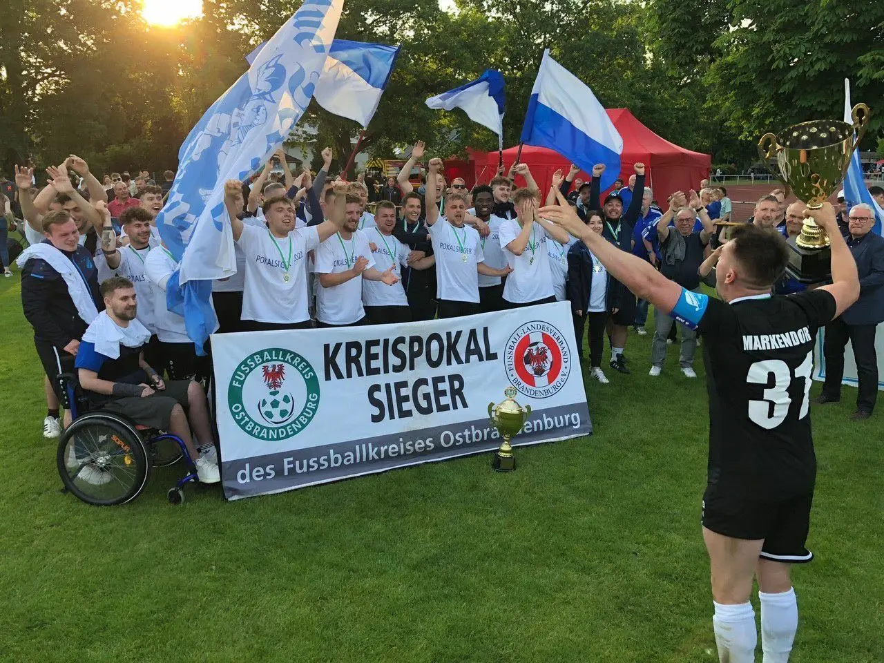 Mannschaftskapitän Alexander Bernwald dirigiert mit dem Pokal seine Mannschaftskameraden vom Kreispokalsieger des FK Ostbrandenburg, Blau-Weiß Markendorf.