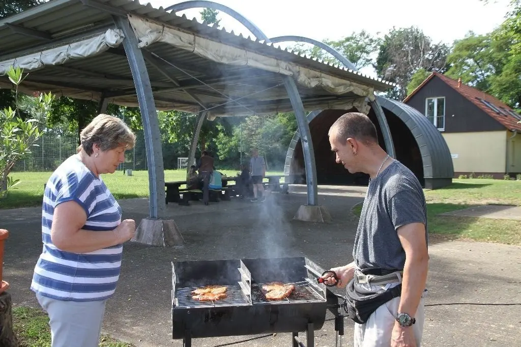Dankeschön-Feier unterm überdachten Festplatz vor Konzertmuschel und Gemeindehaus: Bürgermeisterin Bärbel Mede am Grill mit Wolfgang Wildau, einer der nun scheidenden AGH-Kräfte.