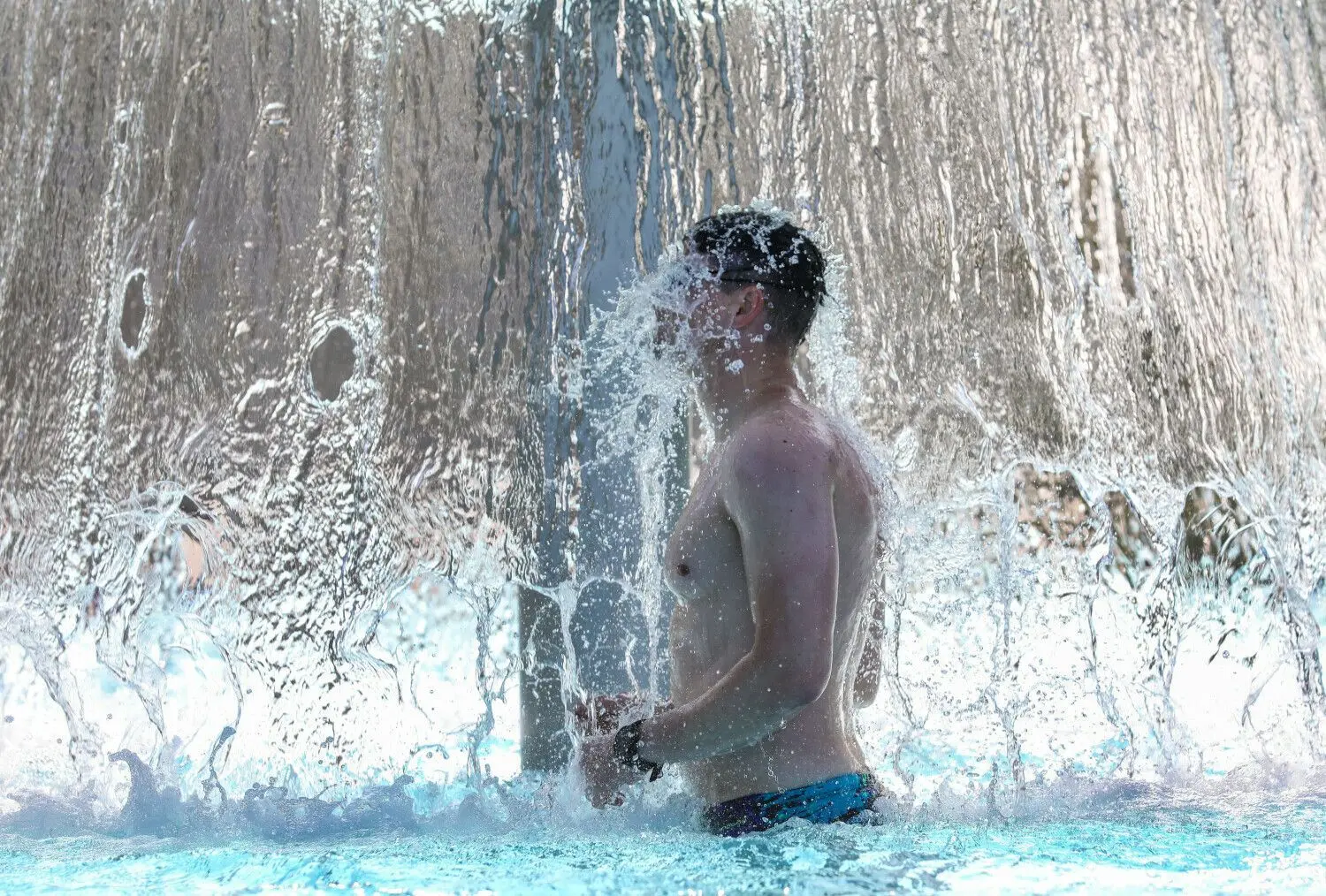 Ein Mann steht in einem Freibad unter einer Wasserfontäne und erfrischt sich (Symbolbild). Am 1. Juni hat das Freibad in Neuzelle geöffnet. In Eisenhüttenstadt beginnt die Freibad-Saison im Inselbad auch noch in dieser Woche.