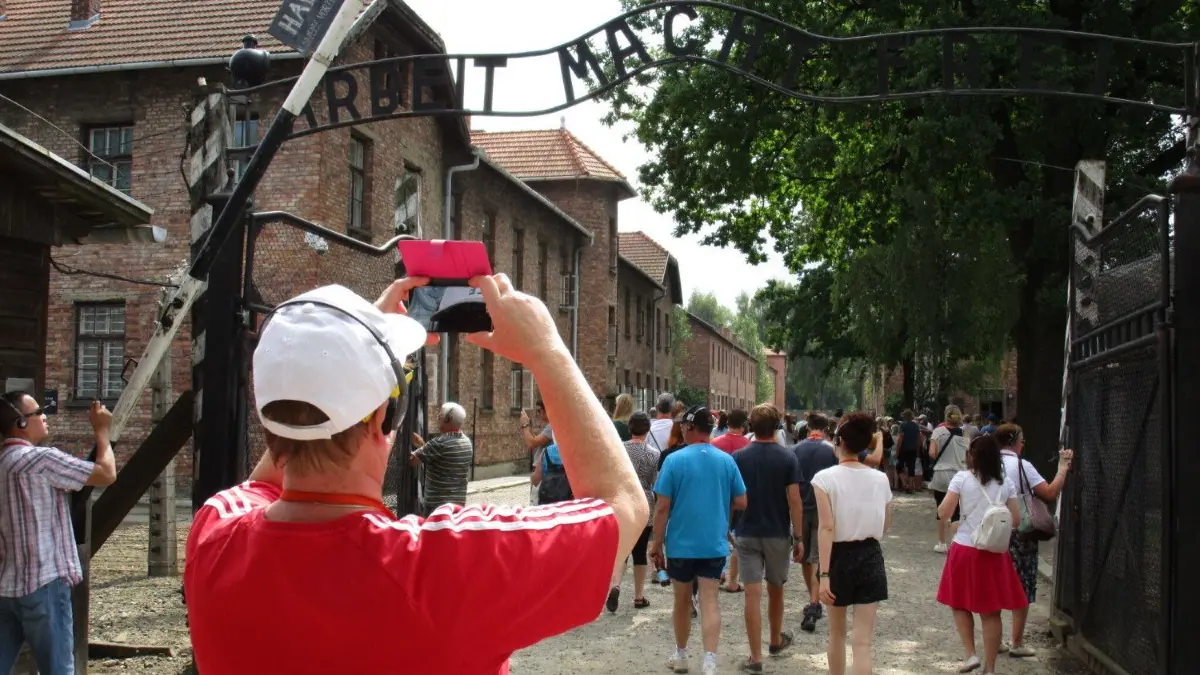 Ein Ort der Trauerarbeit? Das ehemalige Vernichtungslager Auschwitz als Touristenattraktion.
Ein Tourist macht mit seinem Smartphone am 30.07.2014 am Lagertor zum ehemaligen Konzentrationslager in Auschwitz (Polen) ein Foto. Selfies an Orten des Schreckens wie dem einstigen Todeslager Auschwitz provozieren. Der Drang vieler vor allem junger Menschen zur möglichst ungewöhnlichen Selbstdarstellung verdrängt schon mal guten Geschmack. Foto: Klaus Blume/dpa (zu dpa-KORR.: «Selfie in Auschwitz? Selbstdarstellung am Ort des Massenmords» vom 28.08.2014) ++ +++ dpa-Bildfunk +++