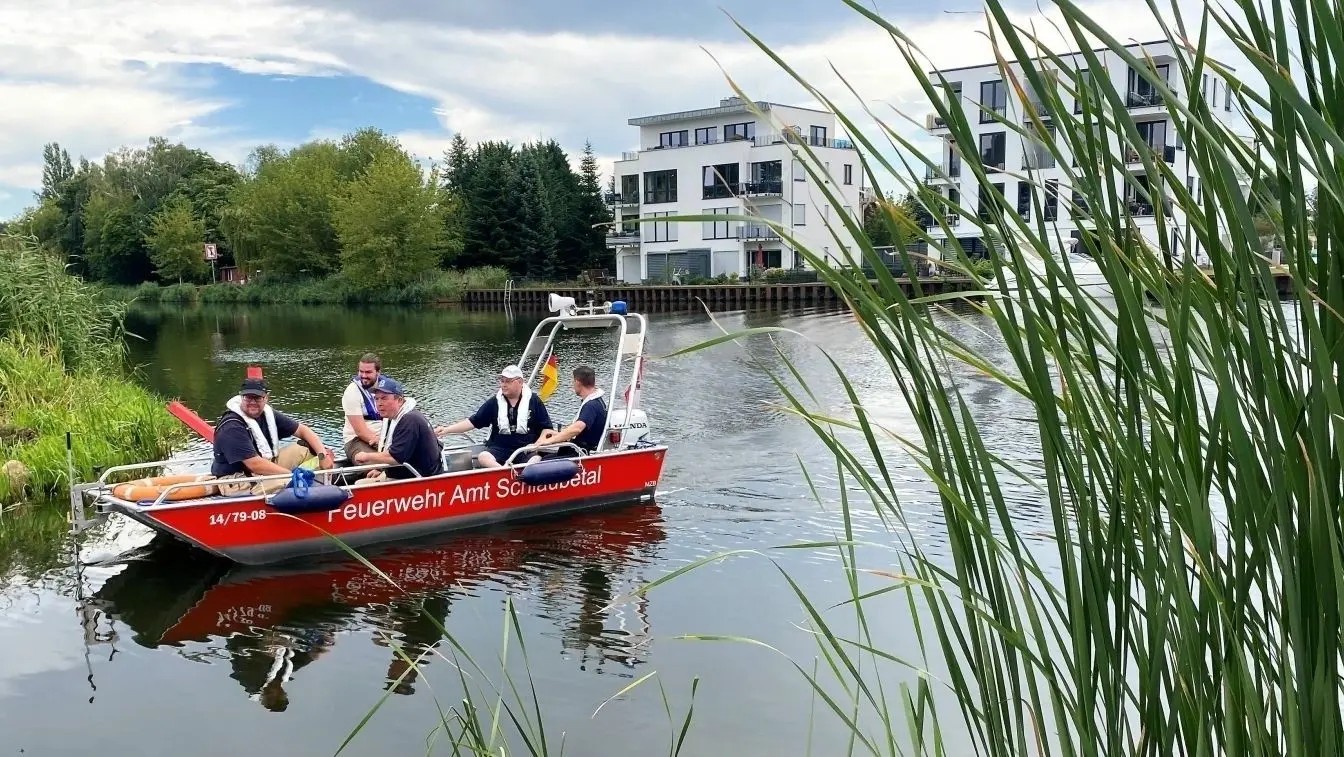 Vermisstensuche: Einsatzkräfte der Amtsfeuerwehr Schlaubetal fahren mit einem Boot den Kleinen Müllroser See in Müllrose ab. Mithilfe eines technischen Gerätes wollen sie eine untergegangene Person aufspüren. Im Hintergrund sind moderne Stadtvillen am Seeufer zu sehen.