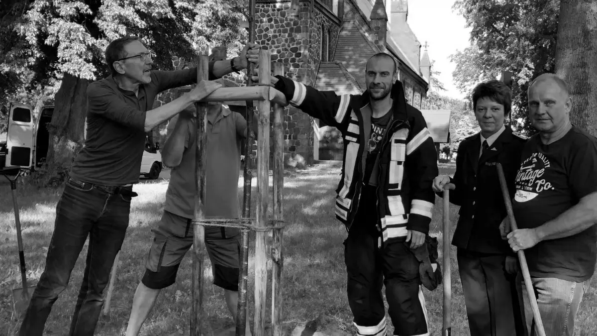 Symbolischer Akt zum Abschluss der Rettungsaktion: Udo Götze (l.) pflanzt mit Mitgliedern des Gemeindekirchenrats und der örtlichen Feuerwehr vor der Kirche eine Winterlinde.
