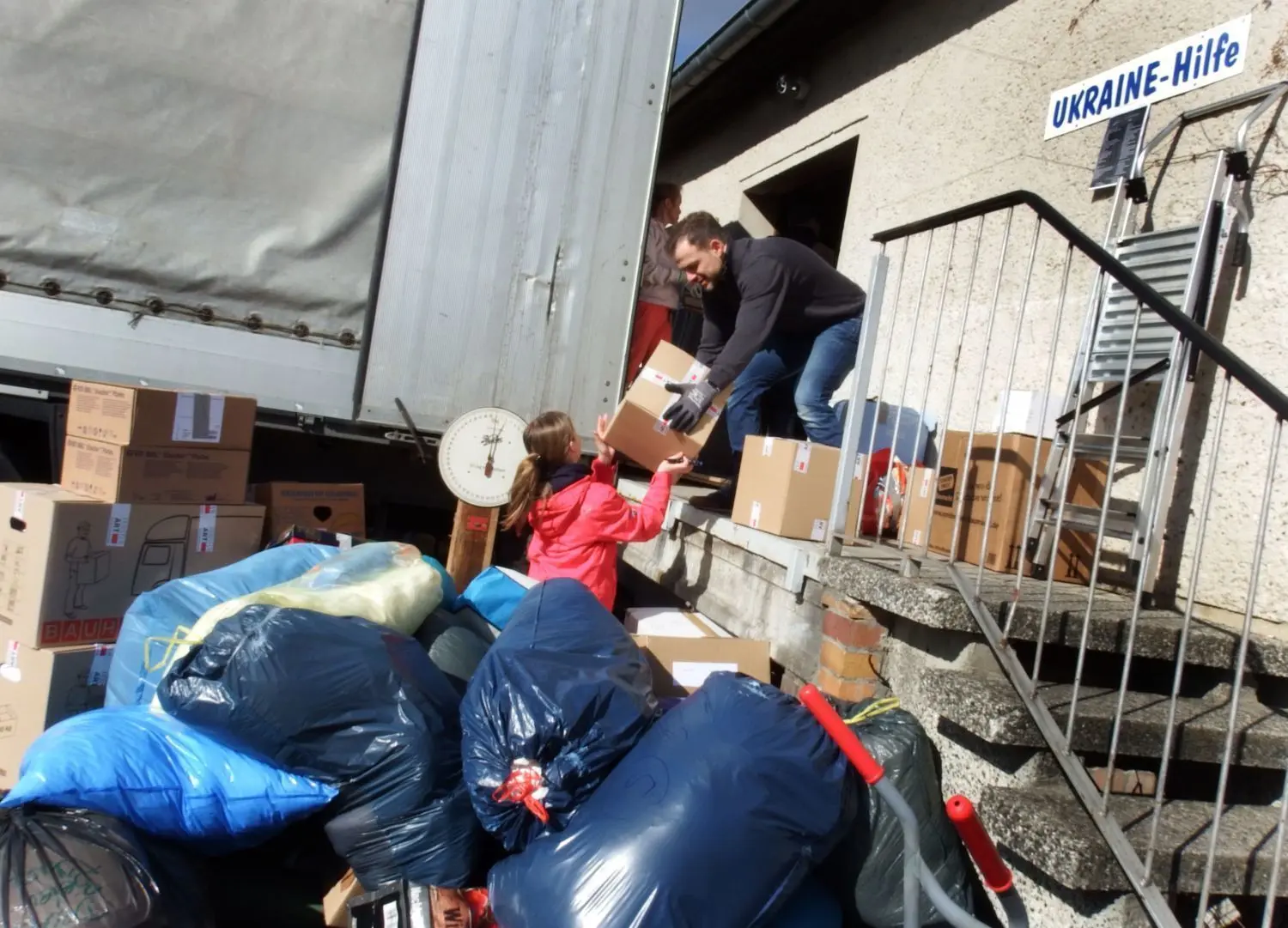 Die kleine Maja reicht ihrem Papa Henry Vogt ein neues Paket. Beide sind aus Ahrensfelde und helfen schon den zweiten Tag in Lobetal beim Beladen von Lkw mit Hilfsgütern für die Ukraine.