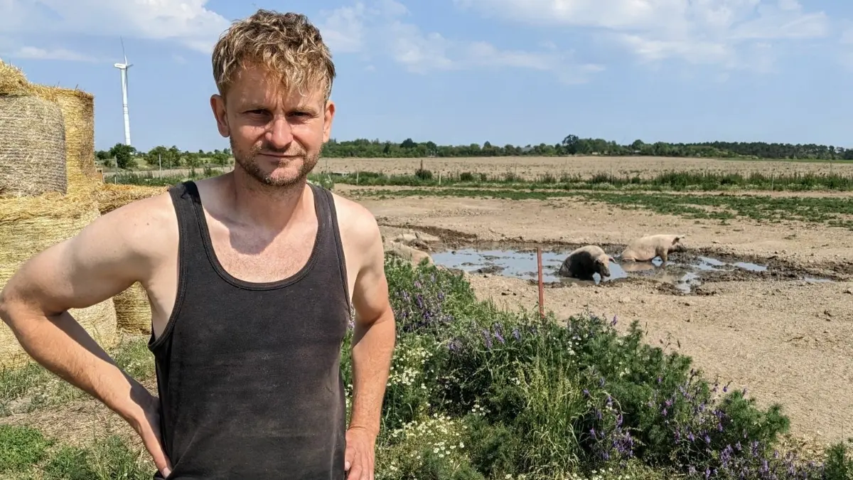Bauer Hans-Christoph Peters aus Werneuchen hat mit allerlei Problemen zu kämpfen. So sorgenfrei wie die Schweine, die sich hinter ihm im Schlamm suhlen, war er schon lange nicht mehr.
Hans-Christoph Peters vom Bauernhof in Löhme (Werneuchen), Bauer Peters am Sauen-Panorama, 8.6.23