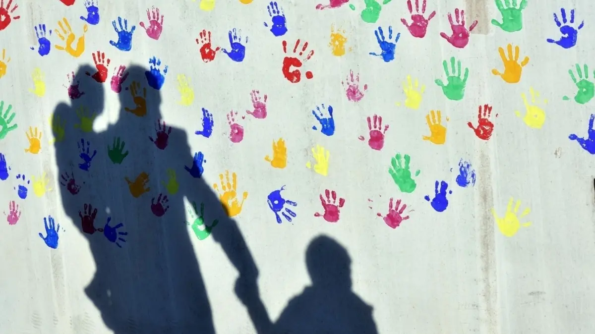 Der sexuelle Missbrauch von Kindern beim DRK in Strausberg wirft seine Schatten auch ins Oderland. Es gibt Schutz-Mechanismen, die in DRK-Kita in Seelow, Bad Freienwalde, Wriezen sowie im Amt Falkenberg-Höhe greifen, aber auch Kritik in Richtung Politik. (Symbolbild)
Ein Mann mit einem Kind auf dem Arm und einem an der Hand wirft einen Schatten auf eine mit bunten Handabdrücken bemalte Wand einer Kindertagesstätte. (zu dpa «Staatsregierung will Kinderschutzambulanz weiter fördern und ausbauen») +++ dpa-Bildfunk +++