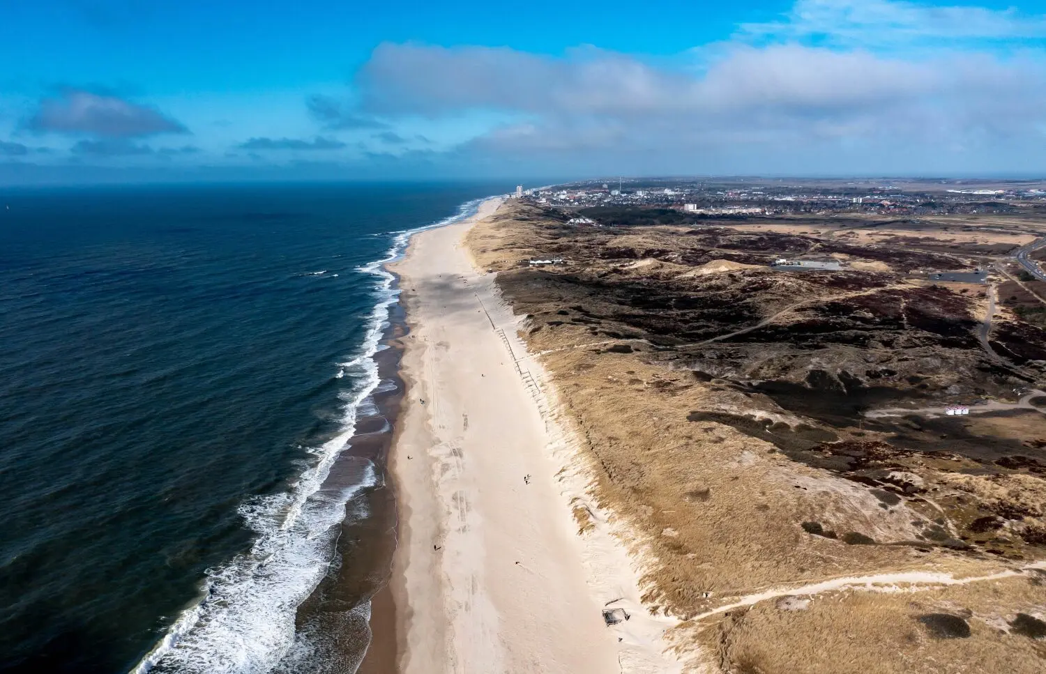 Einige Menschen laufen bei strahlendem Sonnenschein über den Sandstrand der Ostseite der Insel Sylt (im Hintergrund ist die Stadt Westerland zu sehen).