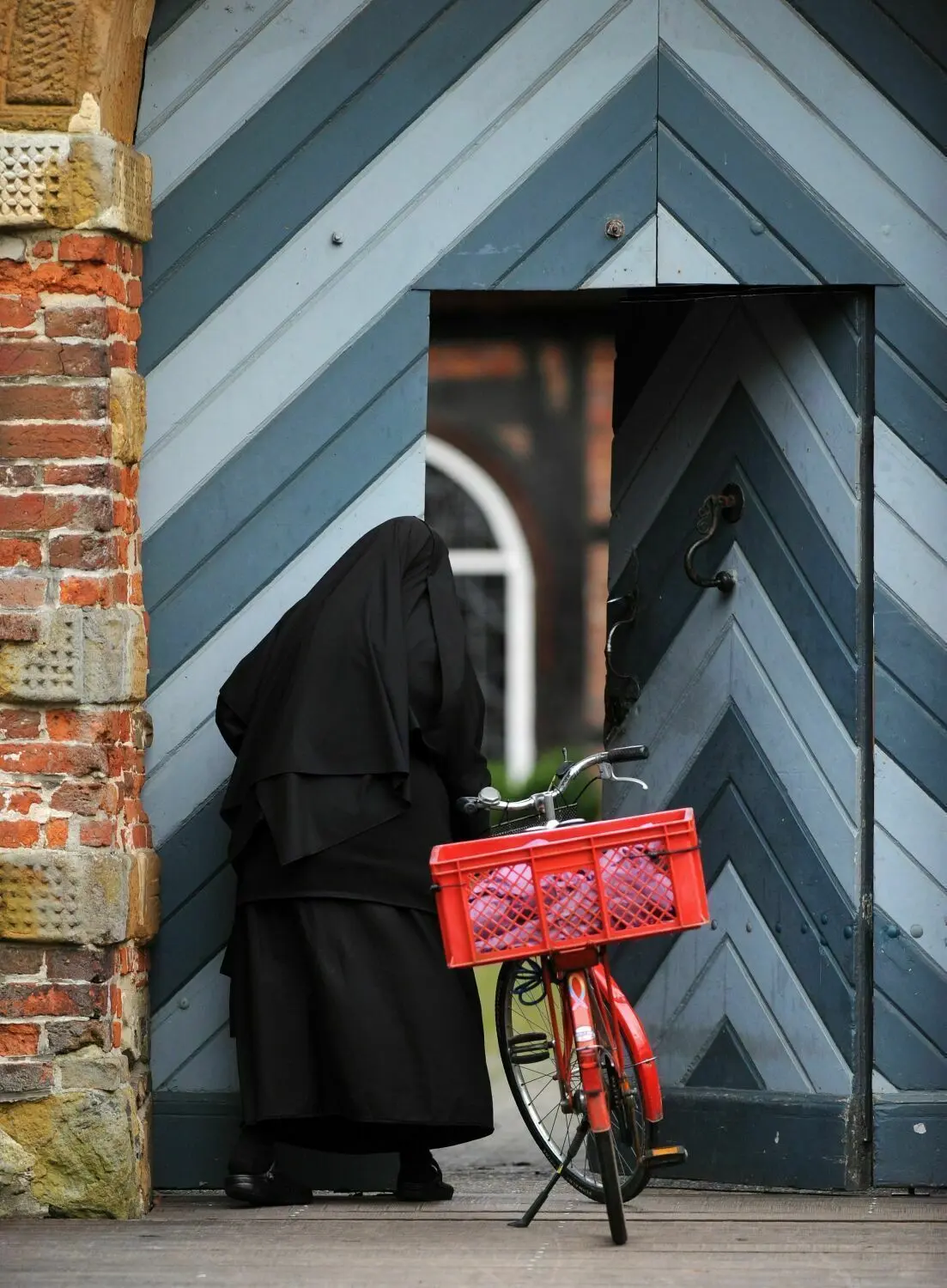Eine Schwester trifft mit ihrem roten Fahrrad vor dem Holztor des Benediktinerklosters von Dinklage (Niedersachsen) ein.