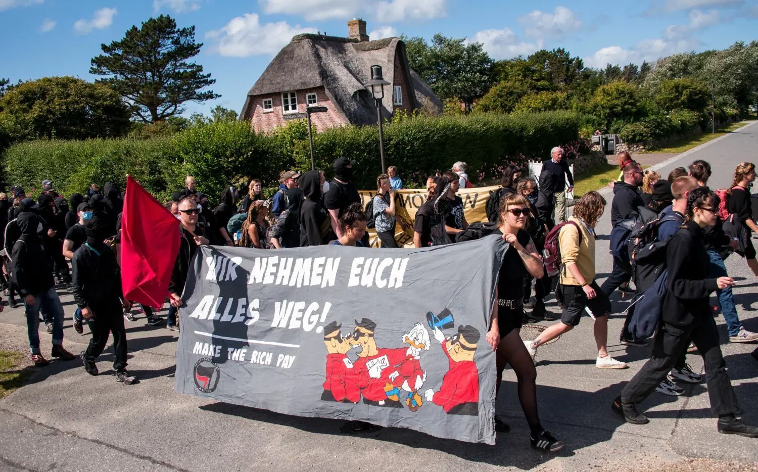 Teilnehmer einer Demonstrantion des Bündnisses "Wer hat, der gibt" halten ein Transparent mit der Aufschrift „Wir nehmen euch alles weg! Make the rich pay“. Das linke Bündnis hat dazu aufgerufen, auf der Insel Sylt für die Umverteilung von Reichtum zu demonstrieren.