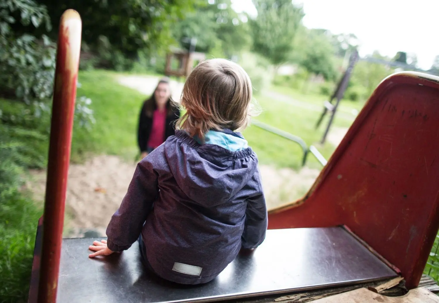 Auch eine Familie – eine kleine: Ein Junge sitzt allein oben auf einer Rutsche, während seine Mutter auf ihn wartet. ⇥