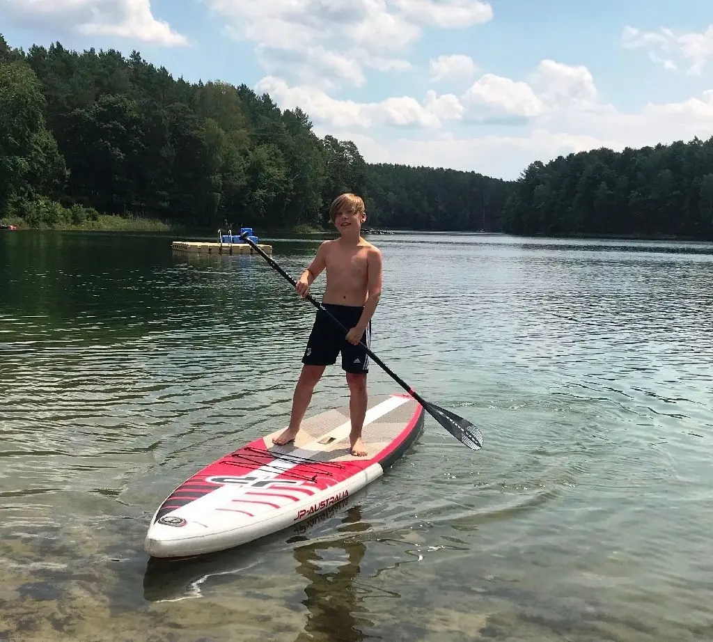 Tony (10) hat sich ein Stehpaddelbrett ausgeliehen und fährt übers Wasser.