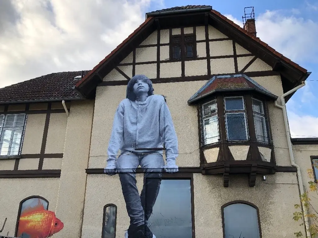 Zierde fürs Stellwerk: Die Aktion "Along the Lines" untersucht das Potential von stillgelegten Stellwerken, um sie langfristig zu Plattformen für Kunst im öffentlichen Raum zu machen. Ein wartendes Kind und ein Goldfisch zieren nun eine Fassade am Bahnhof Erkner.