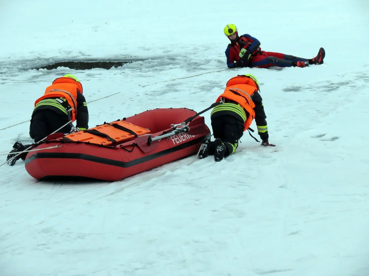 Auf allen Vieren arbeiten sich die Prötzeler Feuerwehrleute Stefan und Sophie Brandt mit dem Schlauchboot zum „verunfallten“ Alan Hübner auf dem Eis vor.