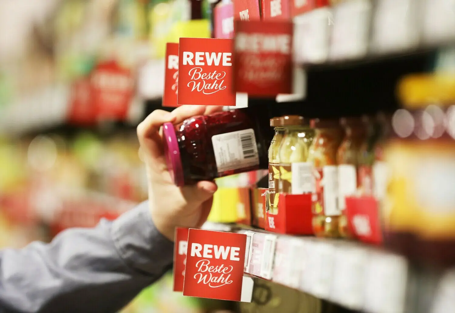 Ein Mann nimmt in einem Supermarkt ein Glas aus dem Regal. Wird in Eisenhüttenstadt demnächst ein Rewe-Markt eröffnet? (Symbolfoto)