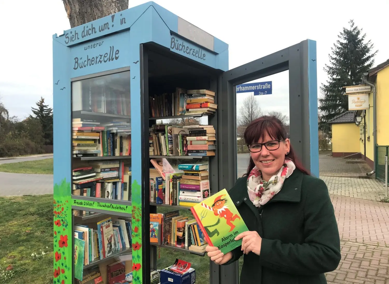 Hat ihr Lieblingskinderbuch gespendet: Michaela Stenzel zeigt an der Bücherzelle das Buch „Alarm im Kasperletheater“.