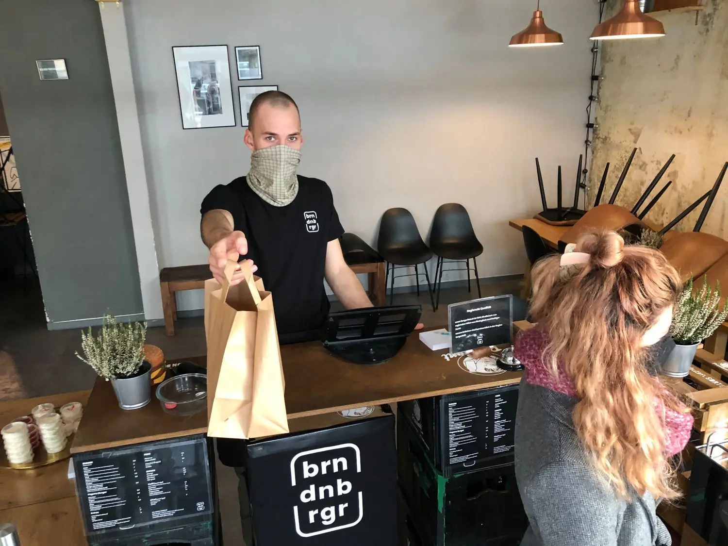 Simon Kamps vom Burger-Restaurant Brndbrgr in der Michaelisstraße reicht eine Papiertüte über den Tresen. Darin verstecken sich heiße Pommes und ein Cheeseburger.