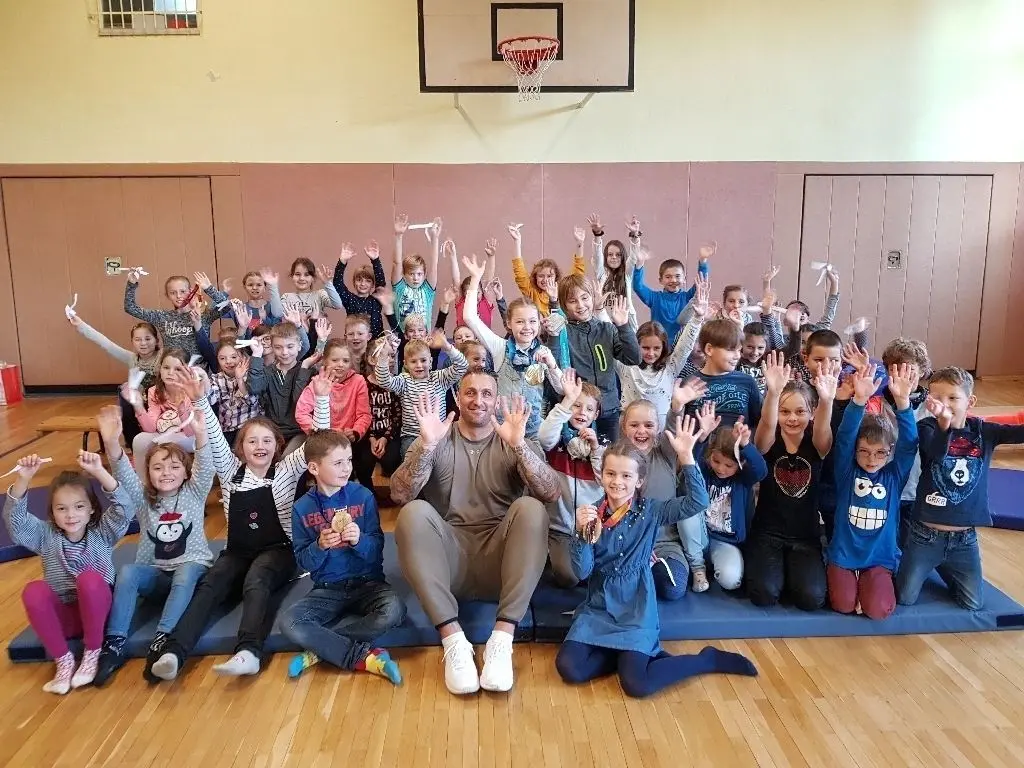 Gold und Silber: Der Ex-Bob-Sportler Kevin Kuske mit Goethe-Grundschülern in der Turnhalle in der Kastanienstraße. Mehr als 50 von insgesamt 163 HortKindern waren dabei. Einige von ihnen halten und tragen Kuskes schwere Gold- und Silbermedaillen.