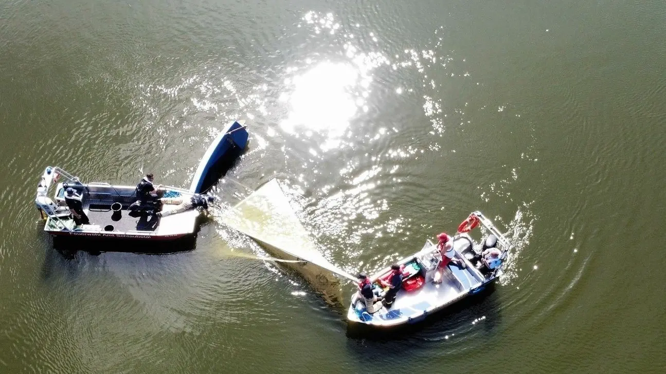 Draufsicht: Mit vereinten Kräften versuchen Einsatzkräfte der Freiwilligen Feuerwehr, ein auf dem Großen Müllroser See gekentertes Segelboot wieder aufzurichten.