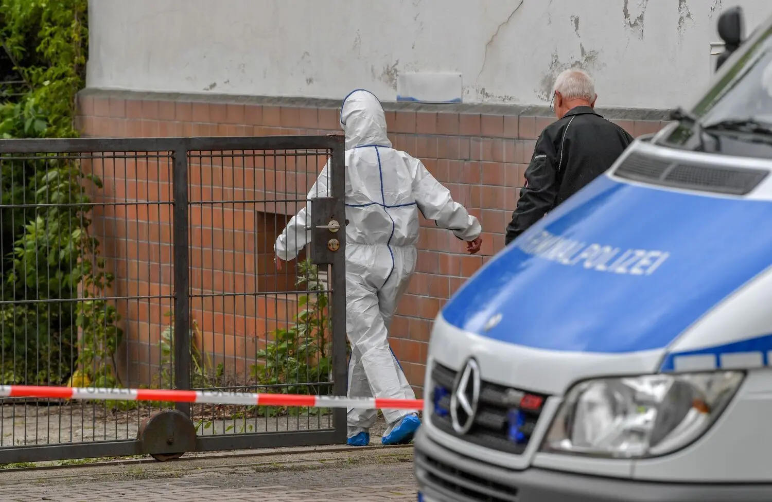 Eine Kriminaltechnikerin im Schutzanzug geht über das Grundstück. Zwei Männer sind Opfer eines brutalen Gewaltverbrechens geworden.