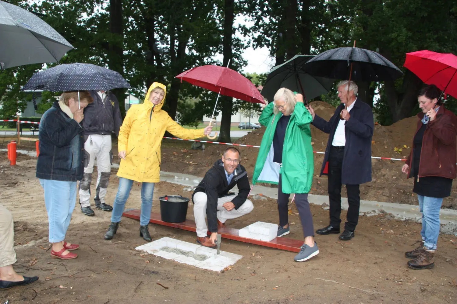 Grundsteinlegung für das Begegnungszentrum in Wolletz: Bürgermeister Frederik Bewer versenkt eine Kapsel mit Münzen, Planzeichnungen und der aktuellen Tageszeitung und legt den ersten Stein. Rechts neben ihm verfolgen Initiatorin Lisa Fiege, Architekt Jan Kleihues und Ortsvorsteherin Kristina Wendt den historischen Moment.