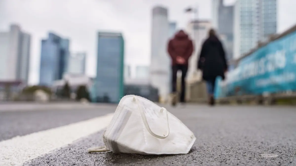 Corona–Zeit: ARCHIV - 18.04.2021, Hessen, Frankfurt/Main: Eine FFP2-Maske liegt auf einem nassen Gehweg in Frankfurt. (zu dpa: «Noch Hunderte Corona-Verfahren bei hessischen Gerichten anhängig») Foto: Frank Rumpenhorst/dpa +++ dpa-Bildfunk +++