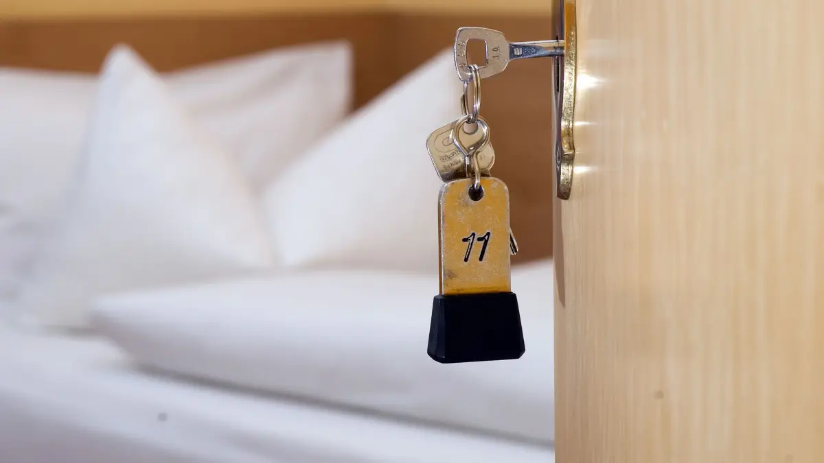 Hotelzimmer: ARCHIV - 27.11.2014, Niedersachsen, Goslar: Ein Zimmerschlüssel hängt am 28.11.2014 in einem Gästehaus vor einem Bett im Türschloss. In NRW sind während der Fußball-EM laut Hotel- und Gaststättenverband noch Betten frei. (zu dpa: «Branchenverband Dehoga: Noch freie Betten zur Fußball-EM in NRW») Foto: Swen Pförtner/dpa +++ dpa-Bildfunk +++