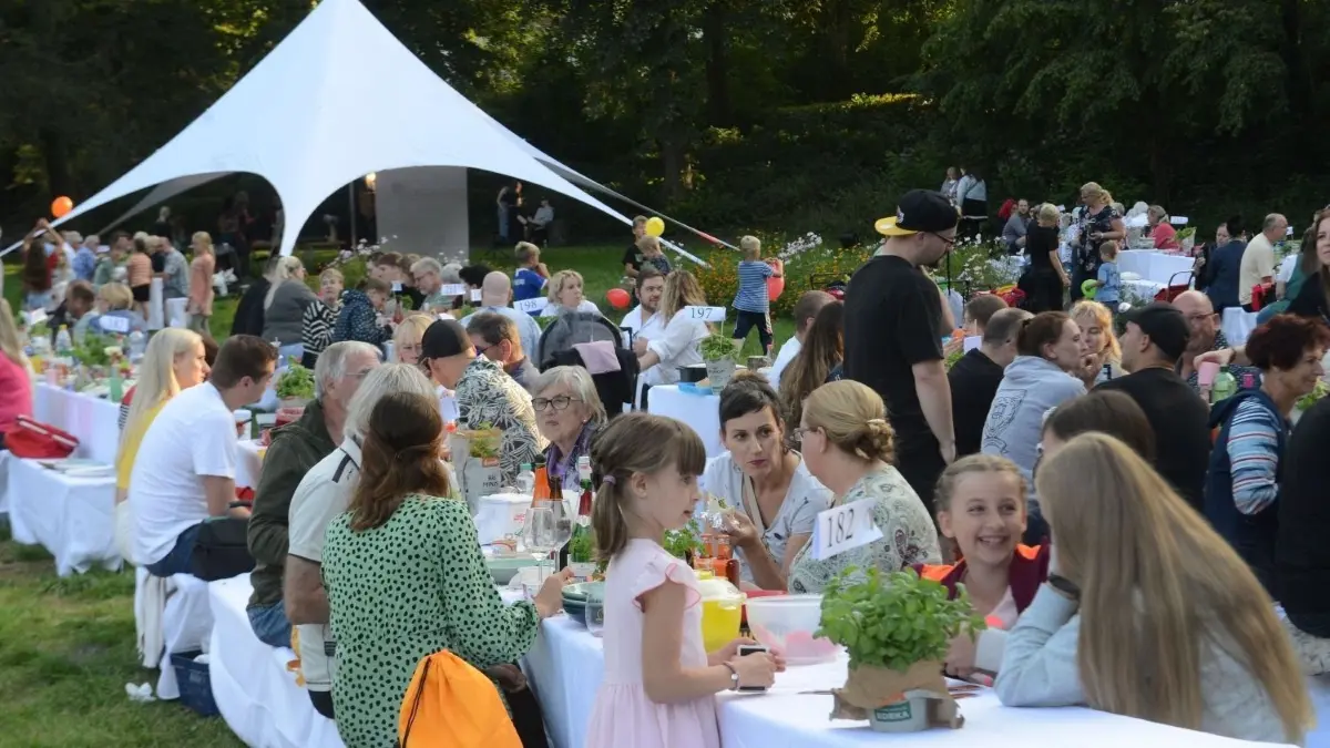 Beim Dinner Picknick im Park der Stadt Bernau bei Berlin, sitzen die Besucher beim mitgebrachten Essen an weiß gedeckten Tischen.