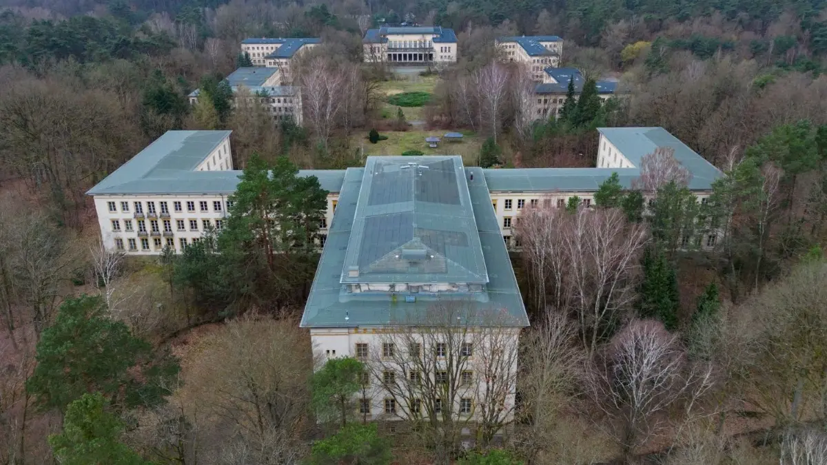 Die Zukunft des Areals am Bogensee bei Wandlitz ist noch ungeklärt. Jetzt hat jedoch das Land Berlin, das Eigentümer des Gebäude–Ensembles ist, mehrere mögliche Nutzungsvarianten vorgestellt.
Das Areal am Bogensee (Luftaufnahme mit einer Drohne). Der Landrat des Landkreises Barnim und der Bürgermeister von Wandlitz haben am 22.03.2024 ein Abrissmoratorium zum Erhalt das Areals Bogensee unterzeichnet. Das nördlich von Berlin gelegene Areal am Bogensee umfasst mit der ehemaligen FDJ-Hochschule Wilhelm Pieck und der Villa von NS-Propagandaminister Goebbels. Die zuletzt wieder sehr intensiv geführte Diskussion zu einem Nachnutzungskonzept Bogensee ist bislang noch ohne Ergebnis und findet nach wie vor wenig Unterstützung durch die Berliner Landesregierung als Eigentümerin des Areals. +++ dpa-Bildfunk +++