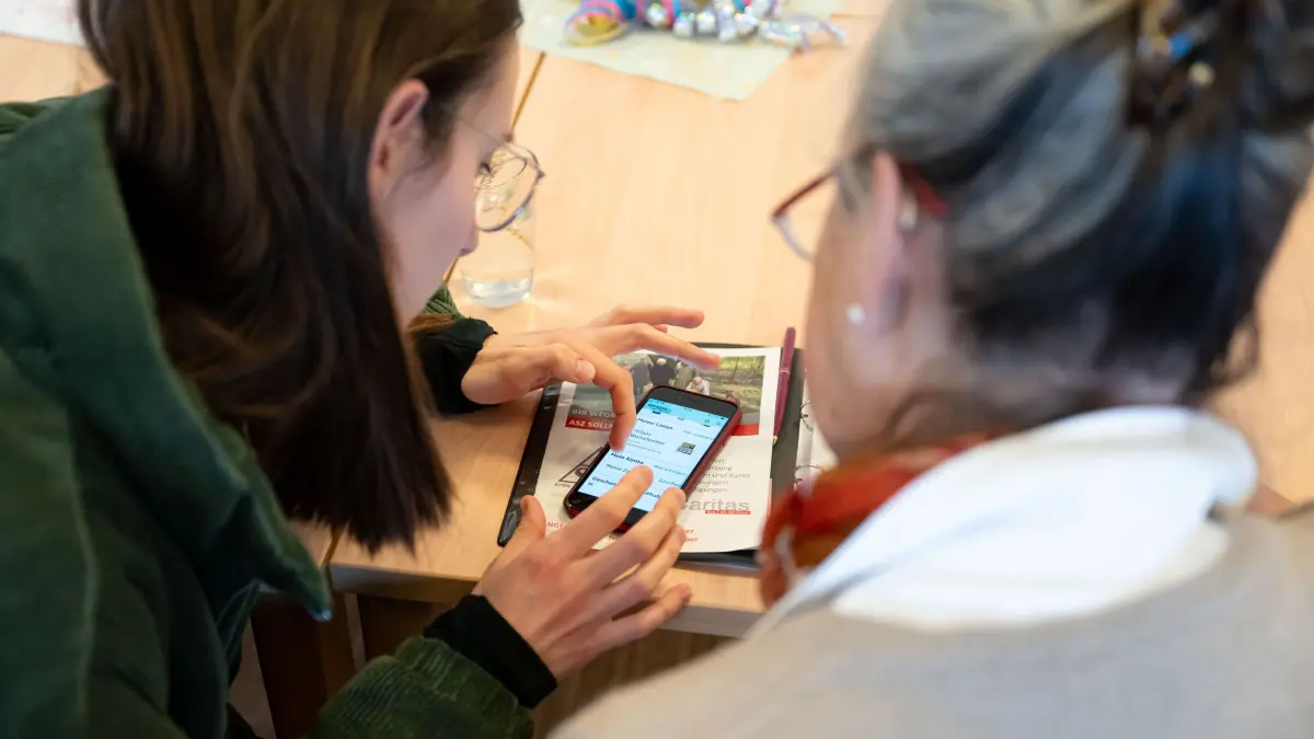 Katrin (L) beantwortet Helga während der Smartphone-Sprechstunde für Senioren Fragen rund um das Apple iPhone. Seit 2021 bietet die Caritas Sprechstunden an, in denen ältere Menschen Hilfe bei Problemen mit dem Handy bekommen. Der Verband sucht dringend nach weiteren Beratern für diese Sprechstunden. (zu dpa: ««Nachhilfe» für das Smartphone: Junge Menschen unterstützen Senioren») +++ dpa-Bildfunk +++