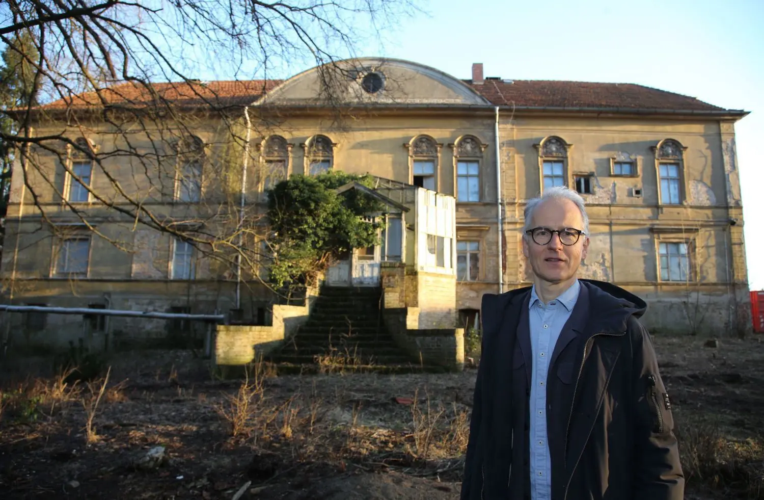 Auf der Rückseite: Gesellschafter Marc Lorenz vor der hinteren Fassade des Gutshauses, die mit Zierelementen und dem zugewachsenen Wintergarten fast märchenhaft wirkt.