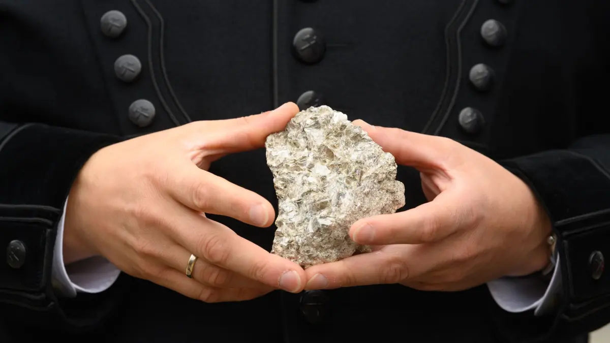 Lithiumabbau im Erzgebirge: ARCHIV - 04.10.2021, Sachsen, Altenberg: Ein Stück mit Lithium durchsetztes Stück Erz hält der sächsische Wirtschaftsminister am "Rohstofftag" in einer Bergmannshabit vor dem Arno Lippmann Schacht in den Händen. In der Region Zinnwald, unter dem Kamm des Erzgebirges an der deutsch-tschechischen Grenze, will das Unternehmen Deutsche Lithium GmbH Bergwerk und eine Aufbereitungsanlage errichten. (Zu dpa: «Sachsen will stärker auf heimische Rohstoffe setzen») (zu dpa: «Sachsen stellt Weichen für Batterieindustrie im Freistaat») Foto: Robert Michael/dpa-Zentralbild/dpa +++ dpa-Bildfunk +++