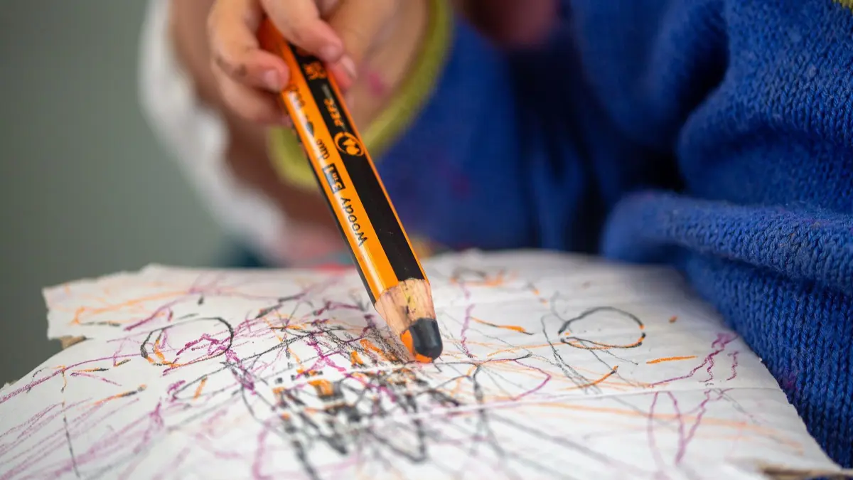 Kleinkind: SYMBOLBILD - 01.07.2023, Berlin: Ein Kleinkind zeichnet auf dem Schoß seiner Mama mit einem Farbstift auf ein Stück Karton. (zu dpa: «Neues Beratungsangebot zur Frühförderung von Kindern mit Behinderungen») Foto: Fernando Gutierrez-Juarez/dpa +++ dpa-Bildfunk +++
