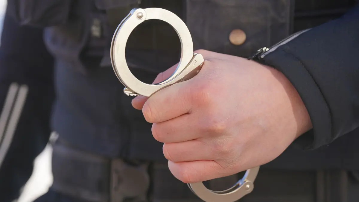 Polizei Handschellen - Symbolbild: ARCHIV - 18.01.2024, Mecklenburg-Vorpommern, Schwerin: ILLUSTRATION - Ein Polizist hält Handschellen in der Hand. (zu dpa: «Toter in Wohnung - Mann und 17-Jährige in U-Haft») Foto: Marcus Brandt/dpa +++ dpa-Bildfunk +++