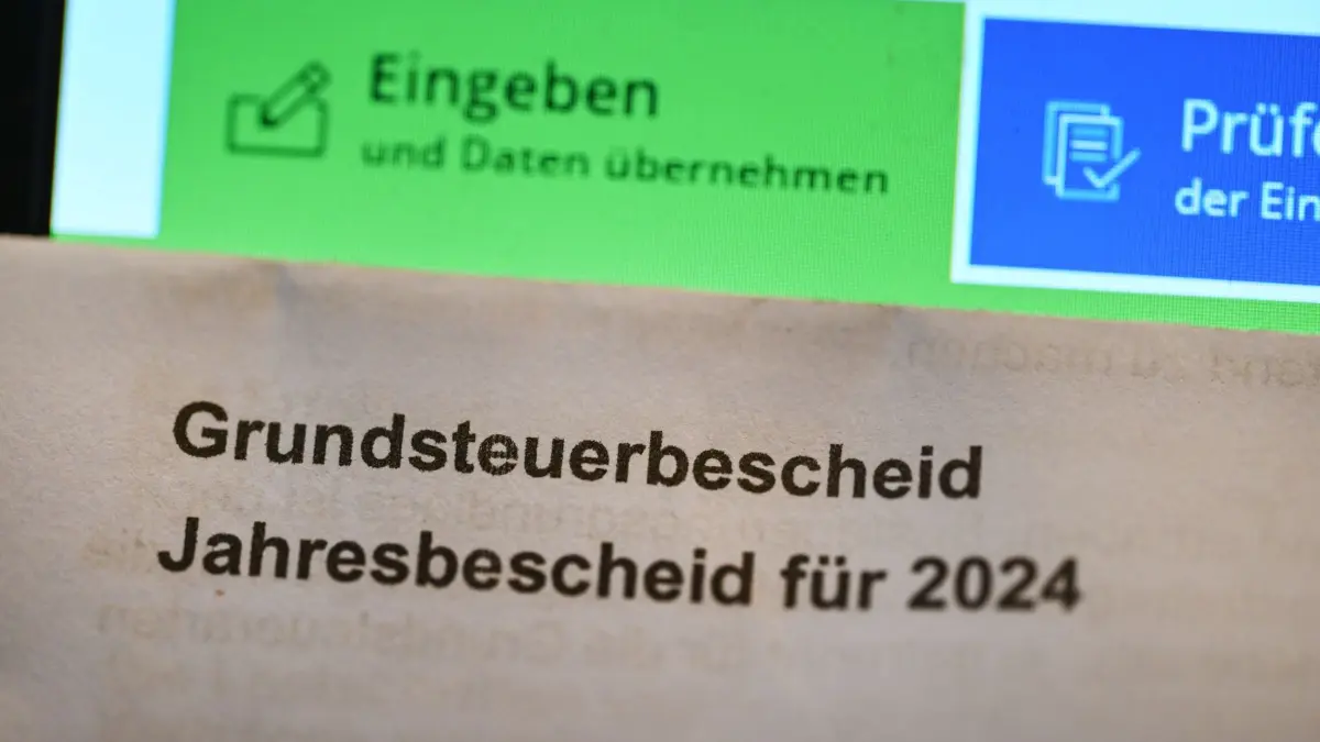 Fast jede zweite Gemeinde hat die Grundsteuer B erhöht: ARCHIV - 18.01.2024, Baden-Württemberg, Stuttgart: Ein Grundsteuerbescheid für 2024 wird vor einen Computerbildschirm gehalten, auf dem ein Formular der Steuerplattform Elster angezeigt wird. Eigentümer müssen sich nach Überzeugung des Bundes der Steuerzahler auf höhere Grundsteuern einstellen. (zu dpa: «Fast jede zweite NRW-Gemeinde hat die Grundsteuer B erhöht») Foto: Bernd Weißbrod/dpa +++ dpa-Bildfunk +++