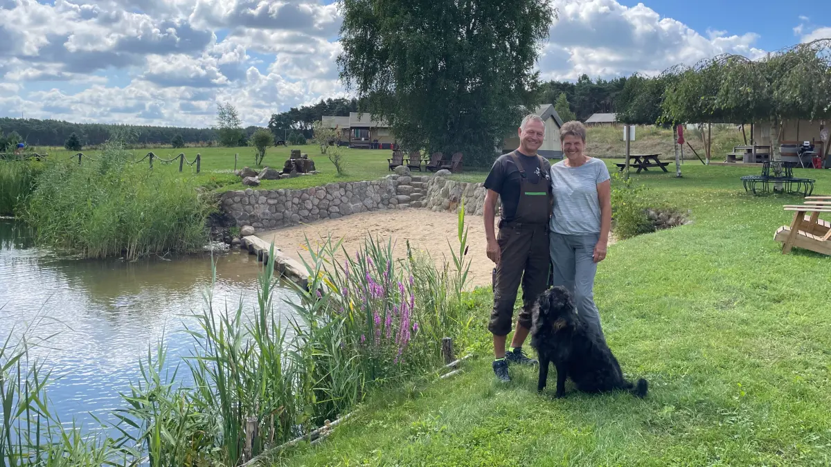 Marion und Michael Werner mit Hund Leo vor dem Naturteich auf dem Glamping-Landgut Voigtsmühle in Friedland, Ortsteil Niewisch.