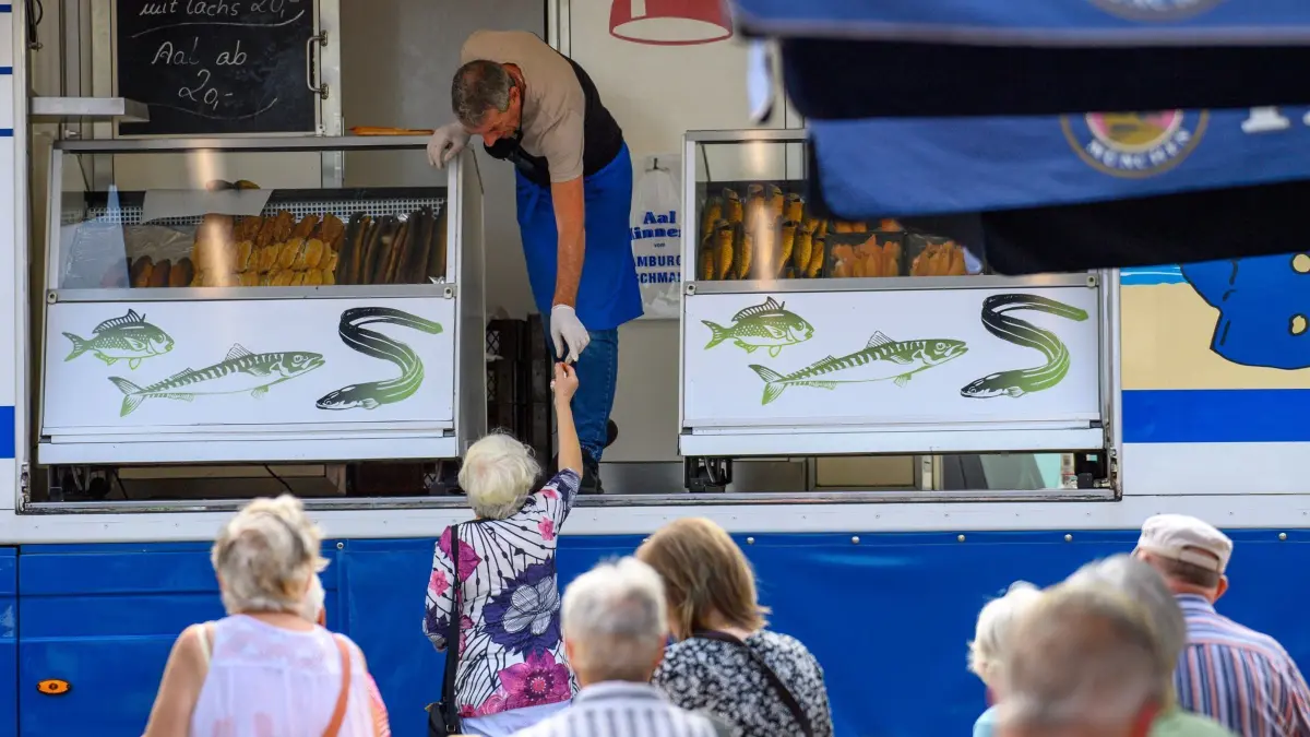 „Echte Gilde der Marktschreier“ in Magdeburg: 16.08.2024, Sachsen-Anhalt, Magdeburg: Heiko Hoffmann alias "Aal Hinnerk" von der "Echten Gilde der Marktschreier" reicht auf dem Alten Markt in Magdeburg einem Marktbesucher ein Stück Lachs zum Probieren. Die Marktschreier-Guilde sind noch bis zum 17. August 2024 auf dem Marktplatz von Magdeburg. Foto: Klaus-Dietmar Gabbert/dpa/ZB - Honorarfrei nur für Bezieher des Dienstes ZB-Funkregio Ost +++ ZB-FUNKREGIO OST +++