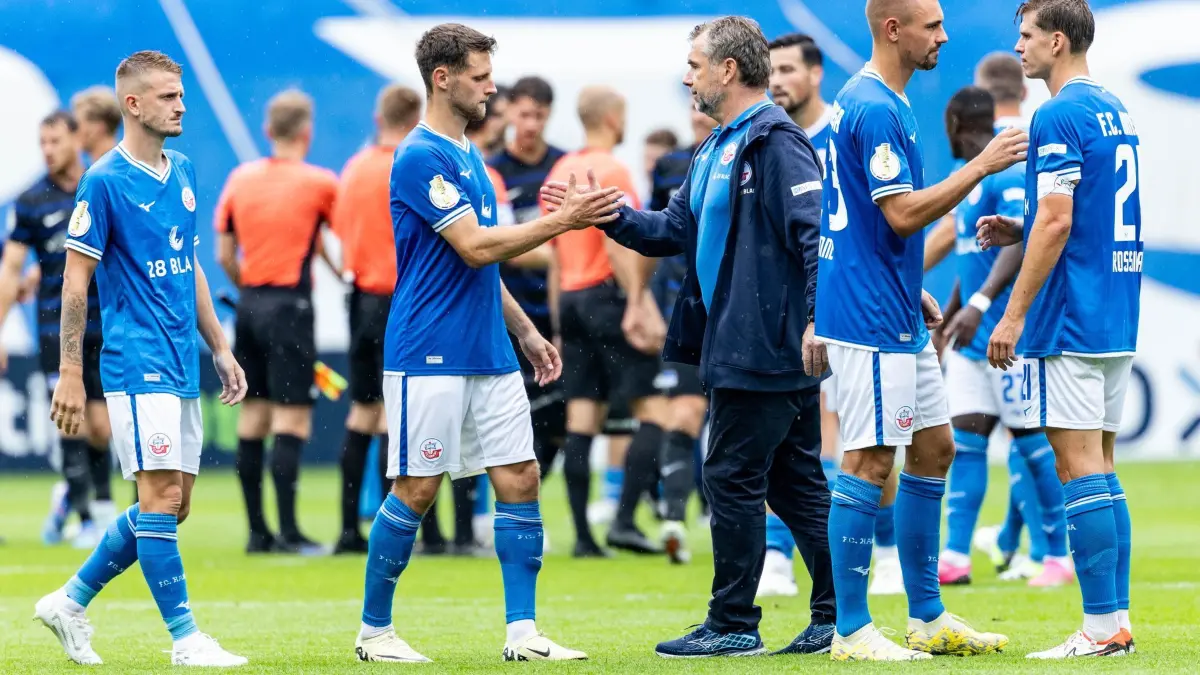 Hansa Rostock - Hertha BSC: 18.08.2024, Mecklenburg-Vorpommern, Rostock: Fußball: DFB-Pokal, Hansa Rostock - Hertha BSC, 1. Runde, Ostseestadion. Rostocks Trainer Bernd Hollerbach (M) gibt seinen Spielern die Hand. Foto: Axel Heimken/dpa - WICHTIGER HINWEIS: Gemäß den Vorgaben der DFL Deutsche Fußball Liga bzw. des DFB Deutscher Fußball-Bund ist es untersagt, in dem Stadion und/oder vom Spiel angefertigte Fotoaufnahmen in Form von Sequenzbildern und/oder videoähnlichen Fotostrecken zu verwerten bzw. verwerten zu lassen. +++ dpa-Bildfunk +++
