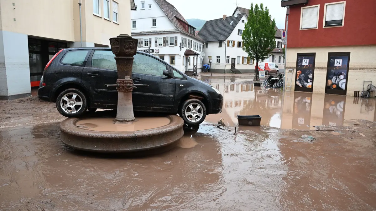 Auf einem Brunnen steht ein durch ein Hochwasser weggespültes Auto.