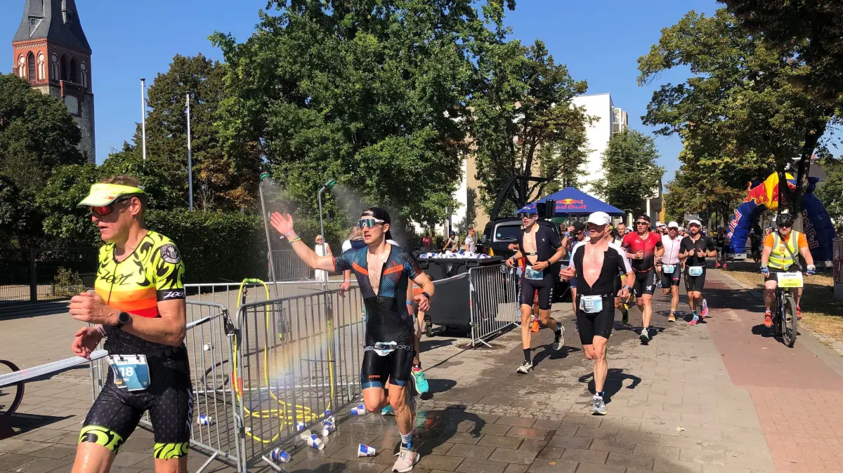 Ironman 70.3. Erkner: Der Halbmarathon führt auch in diesem Jahr am Kirchplatz in Erkner vorbei. Läufer beim Duschen an der Strecke. (Archivfoto 2023)