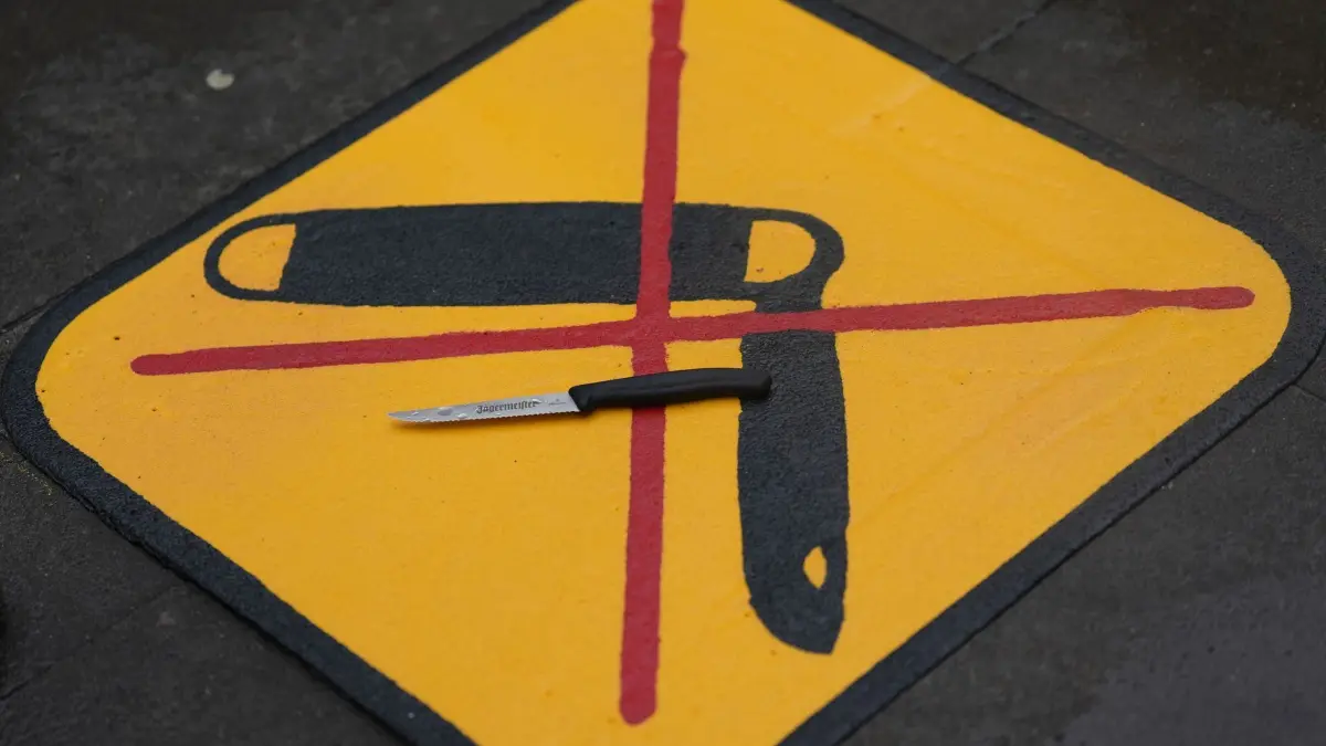 Neue Piktogramme Glasflaschen- und Waffenverbot auf dem Kiez: ILLUSTRATION - 13.11.2024, Hamburg: Ein Messer liegt auf einem Piktogramm zum Messer- und Waffenverbot auf dem Kiez während eines Pressetermins der Polizei in der Talstraße unweit der Reeperbahn. An insgesamt zehn Kiez-Zugängen rund um die Reeperbahn weisen jeweils zwei gelbe Piktogramme auf dem Gehweg, ein durchgestrichenes Messer sowie eine durchgestrichene Glasflasche, auf die Verbote hin. Foto: Marcus Brandt/dpa +++ dpa-Bildfunk +++